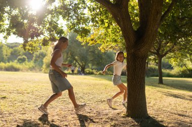 Anne ve kızı güneşli bir parkta birlikte oynuyorlar.