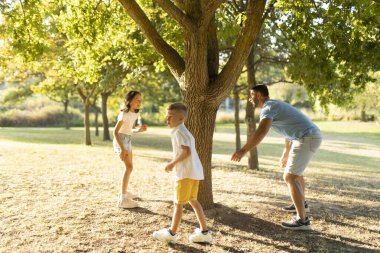 Aile güneşli bir parkta ağaçların altında eğleniyor.