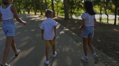 Güneşli bir günde parkta birlikte yürüyen üç çocuk.