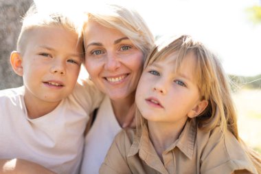 Parlak gün ışığında iki çocuğuyla birlikte gülümseyen anne.