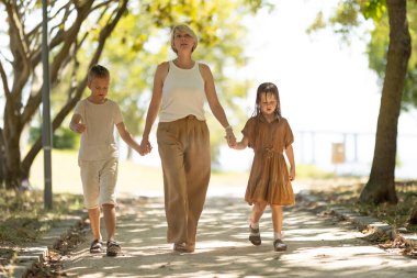 Anne ve iki çocuk ağaçlık bir yolda geziniyorlar.