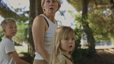 İki çocuklu bir anne, verimli, güneşli bir orman yolunda geziniyor. Huzurlu ve doğal bir ortam, aile birlikteliğini ve açık hava macerasını yansıtıyor.