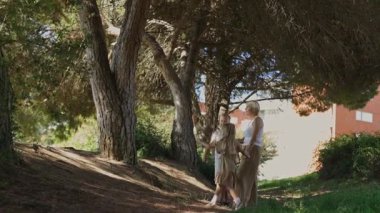 Serene ailesi, ağaçlar ve doğa arasında sıcak ve sevgi dolu bir atmosfer yaratmak için güneşli bir ormanda el ele dolaşır.