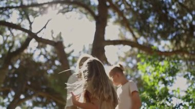 Anne ve çocuklar güneşli bir ormanda sıcak bir kucaklaşmayı paylaşıyorlar, sevgi ve aile bağlarını yakalıyorlar.