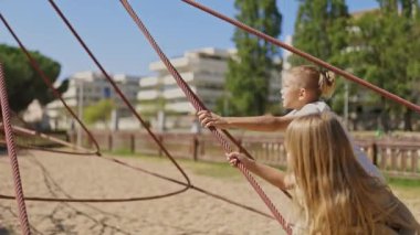 Çocuklar tırmanırken ve oyun alanında sallanırken, güneşli bir parkta oyun oynarken eğleniyorlar.