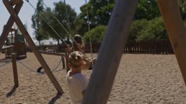 Çocuklar güneşli bir oyun bahçesinde neşeyle salınırlar, açık havada eğlenmenin ve kaygısız çocukluk anlarının özünü yakalarlar.