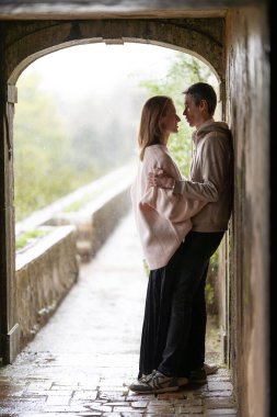 Çift, yağmurdan korunmak için taş tünelde samimi bir anı paylaşıyor.