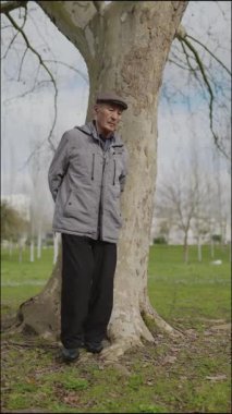 Yaşlı adam parkta huzurlu bir anın tadını çıkarıyor, ağaca yaslanıyor.