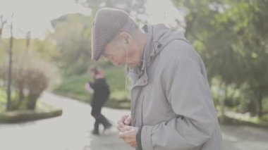 Kulaklık takan yaşlı vatandaş parkta kuşlar için yemek hazırlıyor.