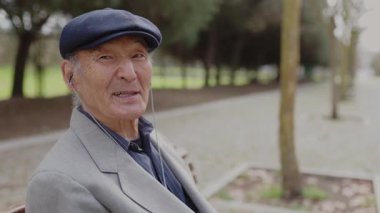 Yaşlı adam bankta oturuyor, kulaklık takıyor ve konuşuyor.