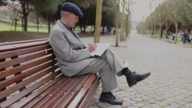 Kıdemli adam bir parkta bankta otururken defterine not alıyor.