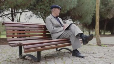 Son sınıf öğrencisi kulaklık takıyor. Parktaki bir bankta otururken not defterine notlar yazıyor.