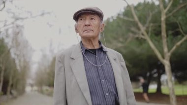 Yaşlı Asyalı adam parkta müzik dinliyor.
