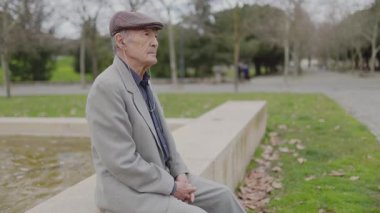 Yaşlı bir adam parktaki bir göletin kenarında derin derin oturuyor.