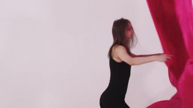 Beyaz stüdyoda pembe bezle oynayan ve dans eden genç güzel bir kadın. Orta çekim