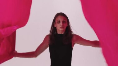 Beyaz stüdyoda pembe bezle oynayan ve dans eden sıska genç bir kadın. Orta çekim