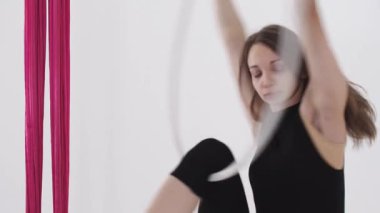 Hava yogası - genç akrobatik kadın tavanın altında asılı duran bir halkayla egzersiz yapıyor - dönüyor. Orta çekim