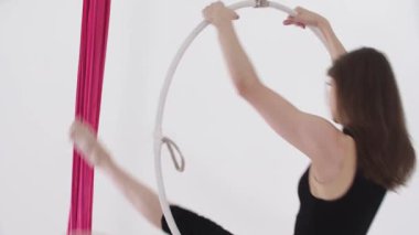 Hava yogası. Tavanın altında asılı halkayla dönen genç bir kadın egzersiz yapıyor. Orta çekim