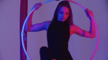 Hava yogası, genç bayan jimnastikçi tavanın altında asılı duran bir çemberin üzerinde dönüyor, neon ışıklı. Orta çekim