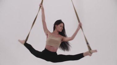 Hava yogası - genç bir kadın kayışlarla dönerken bacaklarını esnetiyor. Orta çekim