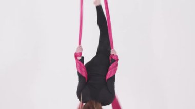 Hava yogası. Pembe kumaş parçasında sallanan ve egzersiz yapan jimnastik yapan bir kadın. Orta çekim