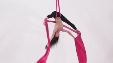 Hava yogası. Pembe kumaş parçasında baş aşağı asılı duran ve egzersiz yapan jimnastik yapan bir kadın. Orta çekim