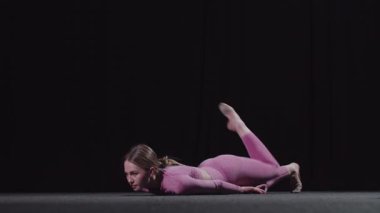 Genç bayan jimnastikçi antrenman için ısınıyor yerde yatıyor ve vücudunu başının üzerine eğiyor. Orta çekim