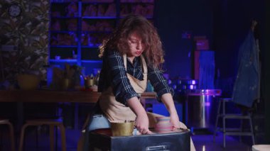 Kıvırcık saçlı bir kadın çömlekçiden saksıyı çıkarıyor. Orta çekim