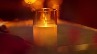 Restoran verandasındaki masada yanan mum. Arka planda masanın başında oturan insanlar. Orta çekim