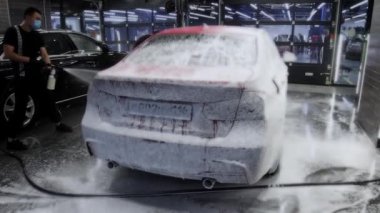 Bir adam sprey kullanarak arabayı köpükle kaplıyor. Orta çekim