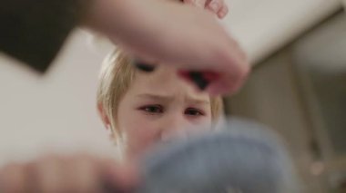 Üzgün çocuk evde annesinin saçını kestiriyor.