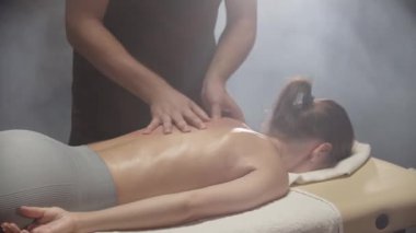 Profesyonel masör spa merkezindeki genç bayana sırt masajı yapıyor.