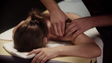 Profesyonel masör, kaplıca salonundaki genç bayanın sırt kaslarına masaj yapıyor.