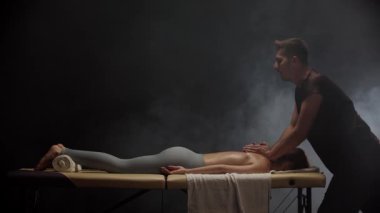 Profesyonel masör masaj masasında yatan genç bir kadına masaj yapıyor.