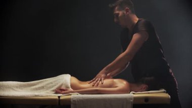Profesyonel masör spa merkezindeki genç bir kadına rahatlatıcı bir sırt masajı yapıyor.