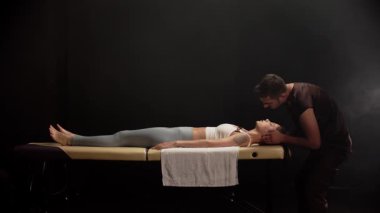 Masör masaj masasında yatan genç bir kadına kafa masajı yapıyor.