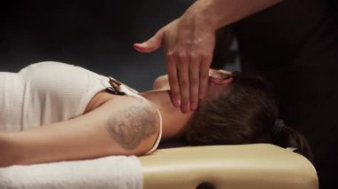 Masör masaj yağı sürüyor ve genç bir kadına boyun masajı yapıyor.