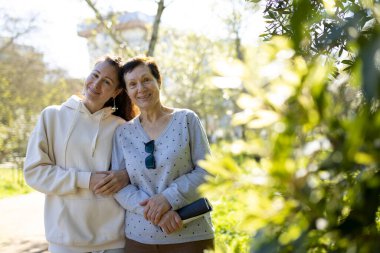 Anne ve kızı parkta güneşli bir günün tadını çıkarıyorlar, kucaklaşıp gülümsüyorlar.