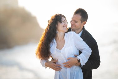 Romantik çift gün batımında kumsalda kucaklaşıyorlar, birlikte hassas bir anın tadını çıkarıyorlar.