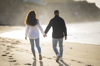 Romantik çift gün batımında kumlu sahilde sakin bir gezinti yapıyor.