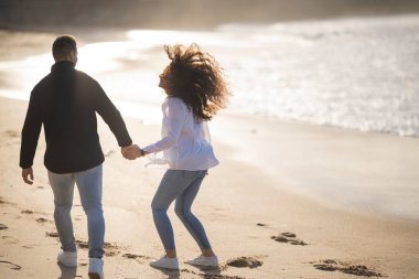 Romantik çift gün batımında kumlu bir sahilde el ele tutuşuyor ve birlikte tasasız bir tatilin tadını çıkarıyorlar.
