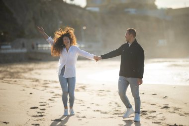 Kaygısız çift romantik bir anın tadını çıkarıyor, gün batımında sahilde koşuyorlar.