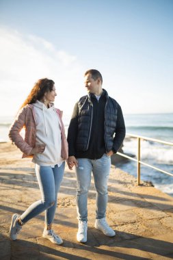 Romantik çift birlikte huzurlu bir anın tadını çıkarıyor, el ele tutuşuyor ve güneşin doğuşundaki güzel okyanus manzarasına hayran kalıyorlar.