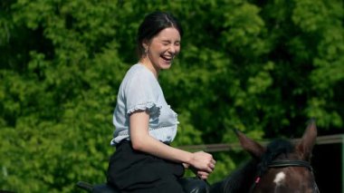 Genç bir kadın ata biniyor ve gülümsüyor.