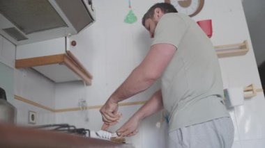 Günlük kıyafet giyen bir adam mutfak tezgahında ekmek keser.