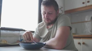 Sıradan bir yetişkin adam mutfağında kahvaltı gevreğinin tadını çıkarıyor.