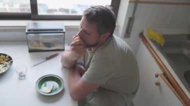 Üzgün adam mutfak zemininde oturmuş elma yiyor.