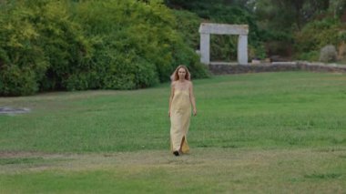 Sarı elbiseli bir kadın parkta yürüyor.