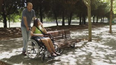 Adam parkta tekerlekli sandalyede bir kadını itiyor, ağır çekimde yakalanmış.