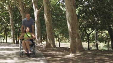 Adam parkta tekerlekli sandalyede bir kadını itiyor.